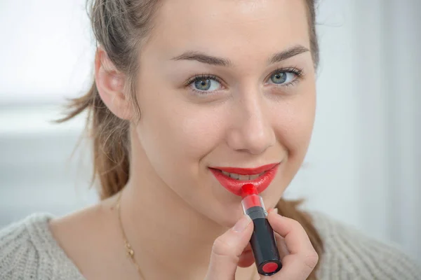 Nuori ja hymyilevä nainen laittaa huulipunaa — kuvapankkivalokuva