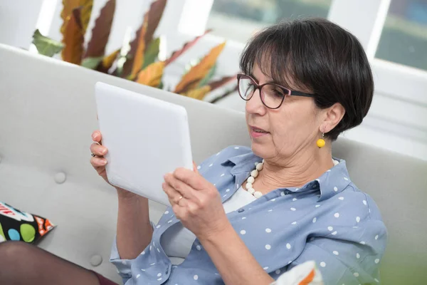 Зрелая брюнетка женщина сидит на диване с помощью цифрового планшета — стоковое фото