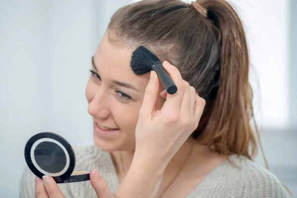 Giovane e sorridente donna applicando polvere sul suo viso — Foto Stock