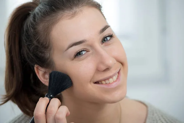 Junge und lächelnde Frau, die Puder auf ihr Gesicht aufträgt — Stockfoto