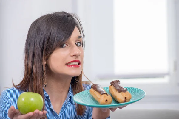 Junge Frau hat die Wahl zwischen einem Apfel und Schokoladengebäck — Stockfoto