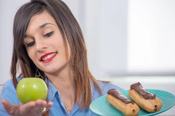 Jeune femme au choix entre une pomme et une pâtisserie au chocolat — Photo