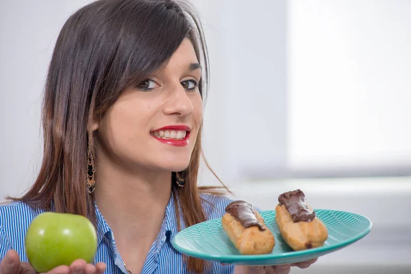 Jeune femme au choix entre une pomme et une pâtisserie au chocolat — Photo