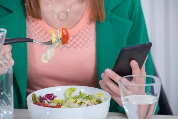 Nuori nainen syö salaattia ja puhelin — kuvapankkivalokuva
