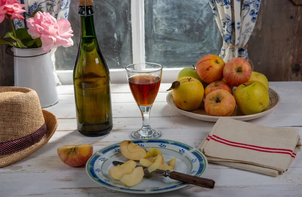 Bottle and glass of cider with apples. In rustic house, window b — Stock Photo, Image