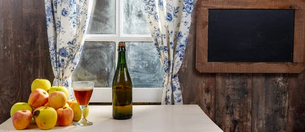 Botella y vaso de sidra con manzanas. En casa rústica, ventana b — Foto de Stock