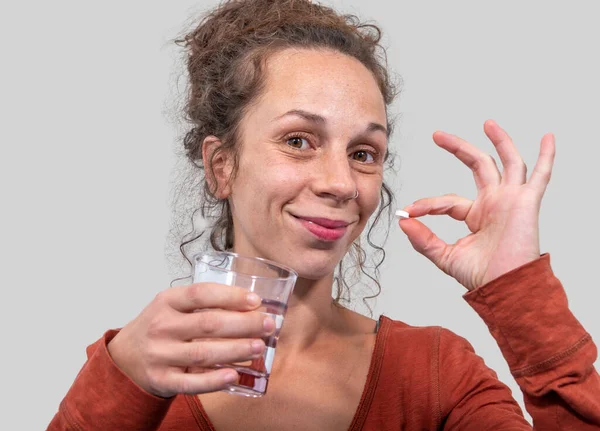 Mujer feliz sosteniendo una píldora redonda blanca y un vaso de agua mirada — Foto de Stock