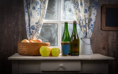 Elmalı şişe ve bir bardak elma şarabı. Pencerenin yanında, pas içinde.