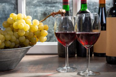 İki şarap kadehi, üzüm ve kırmızı şarap şişeleriyle kompozisyon.