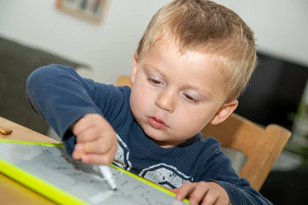Ένα δίχρονο αγόρι ζωγραφίζει σε λευκό πίνακα στο σπίτι.. — Φωτογραφία Αρχείου