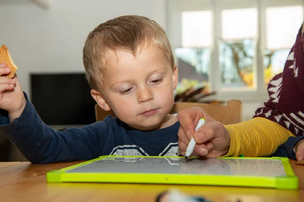 Två år gammal pojke ritar på vit tavla hemma. — Stockfoto