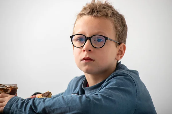 Задумчивый мальчик в очках ест шоколад — стоковое фото