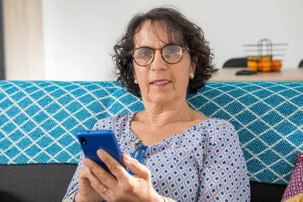 Cheerful brunette senior woman using smartphone while sitting on — Stock Fotó