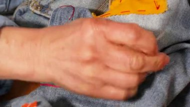 Yaşlı kadın elleri kumaş ve iğne dikiyor. Yaşlı kadın eli pantolon dikmiş., 
