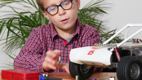 小さな男の子が家でモデル無線制御車を修理し — ストック動画