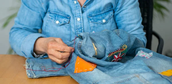 an elderly woman hands sewing on fabric jeans,