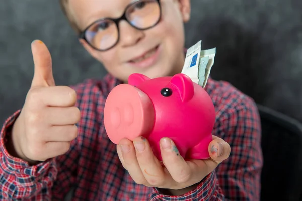 微笑带着眼镜的小男孩把钱投入一个存钱罐 — 图库照片