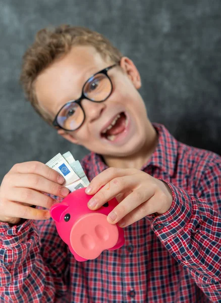 一个戴眼镜的有趣的小男孩把钱存进了储蓄罐 — 图库照片