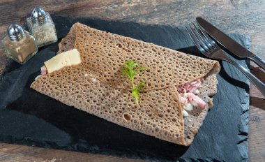 Siyah bir levhada peynirli ve pastırmalı Breton krepi.