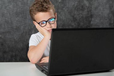 Ciddi bir çocuk dizüstü bilgisayarla oturuyor.