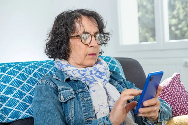 Wesoły Brunetka Senior Kobieta Pomocą Smartfona Podczas Siedzi Kanapie — Zdjęcie stockowe
