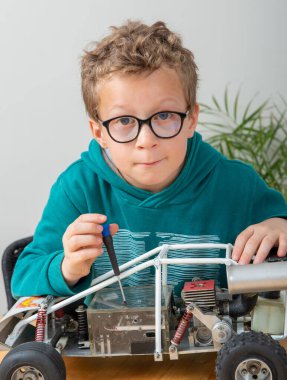 Evde uzaktan kumandalı model bir arabayı tamir eden küçük bir çocuk.