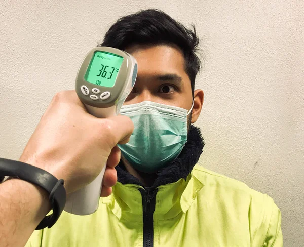 Hand holding infrared thermometer to measuring temperature on asia people with face mask on background. Covid flu screening 19 concept.