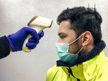 Arka planda yüz maskesi olan Asyalıların sıcaklığını ölçmek için el ele tutuşan kızılötesi termometre. Grip taraması 19 konsept.