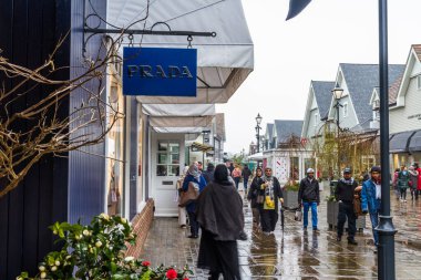 Editör, yağmurlu bir günde alışveriş yapanlar Bicester Village Outlet
