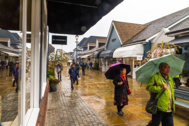 Editör, yağmurlu bir günde alışveriş yapanlar Bicester Village Outlet