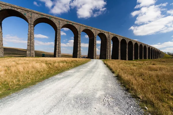 Path leading to sunlit arches of a railway viaduct, wide angle — Stock Photo, Image