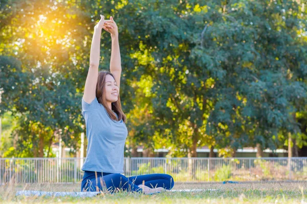 Young asian smiling woman practicing yoga, sitting in easy pose at park. — Stock Photo, Image