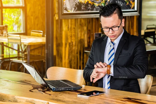Hombre de negocios asiático mirando reloj de pulsera mientras trabaja con el teléfono inteligente y el ordenador portátil . — Foto de Stock
