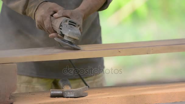 Ξυλουργός συνεργάζεται με ένα ηλεκτρικό τρίφτη και επεξεργάζεται ξύλινα προϊόντα. Ξυλουργός με τον φορητό ηλεκτρικό τρίφτη στα χέρια για την ξυλουργική. — Αρχείο Βίντεο