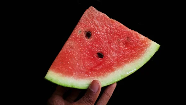 Siyah arka planda karpuzu dilimlenmiş halde tutan adam.