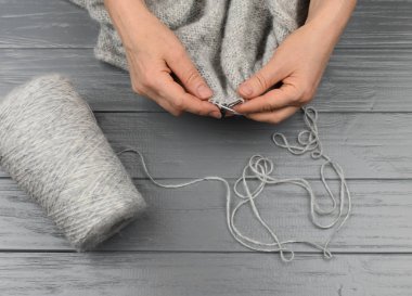 Kadın eli, yakın plan örüyor. Gri yün keten ve gri ahşap arka planda bir bobbin iplik. Yukarıdan bak. El yapımı..
