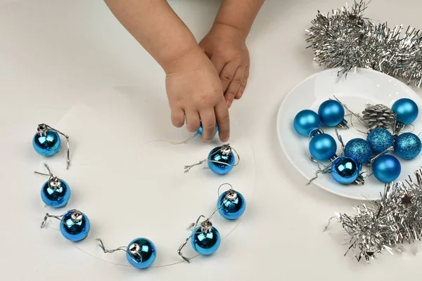 Τα χέρια των παιδιών φτιάχνουν χριστουγεννιάτικο παιχνίδι. Ασημένια καρφίτσα και χτύπημα, μπλε μπάλες Χριστουγέννων. — Φωτογραφία Αρχείου