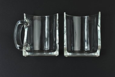 Siyah arka planda kırık cam bardak. Kırık bir bardağın iki yarısı siyah bir masada yatıyor..