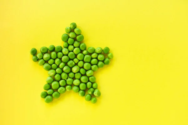 Estrela colocada de ervilhas verdes em um fundo amarelo . — Fotografia de Stock