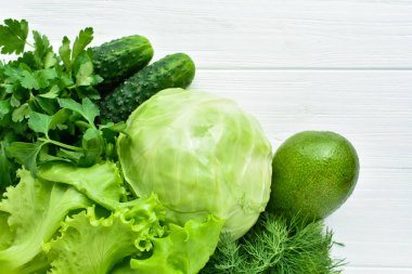 Green vegetables on white wooden background. Salad, cabbage, cucumber, dill, parsley, avocado.