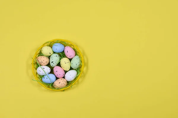 Œufs de Pâques multicolores dans un panier jaune sur fond jaune. Place pour une inscription. Vue d'en haut. Pour les cartes postales. Concept de Pâques . — Photo