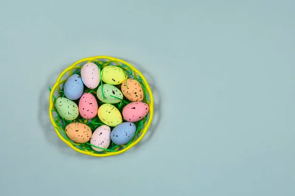 Multi-colored Easter eggs in a yellow basket on a blue background. Place for an inscription. View from above. For greeting cards. Easter concept. — Stock Photo, Image