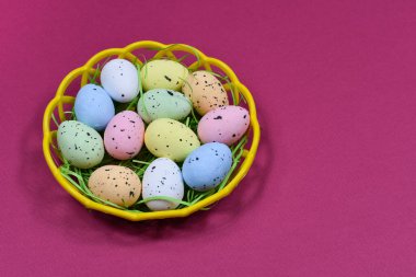 Multi-colored Easter eggs in a yellow basket on a dark pink background background. Place for an inscription. View from above. Easter concept.