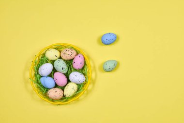 Multi-colored Easter eggs in a yellow basket on a yellow background. Place for an inscription. View from above. For postcards. Easter concept.