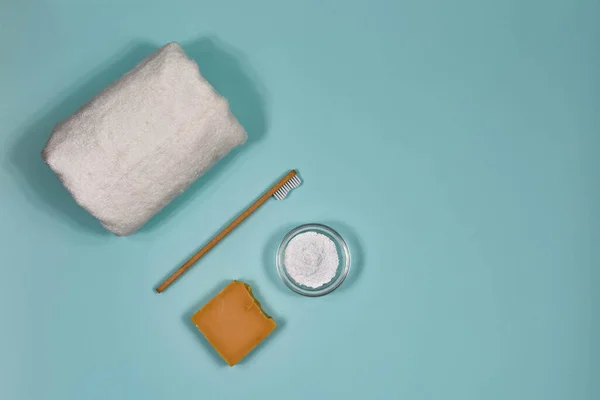 Toothbrush, toothpowder, towel and soap on a blue background. Eco-friendly bamboo toothbrush.