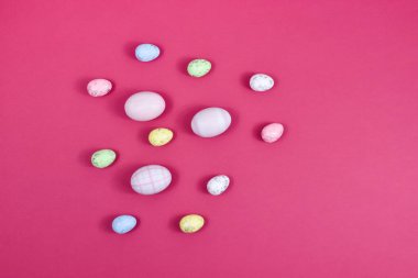 Paskalya konsepti. Paskalya yumurtaları, beyaz bir duvarın arka planında kırmızı bir masanın üzerinde beyaz çiçekli bir sepetin yanında. Yazı için uygun bir yer. Tebrik kartları için..