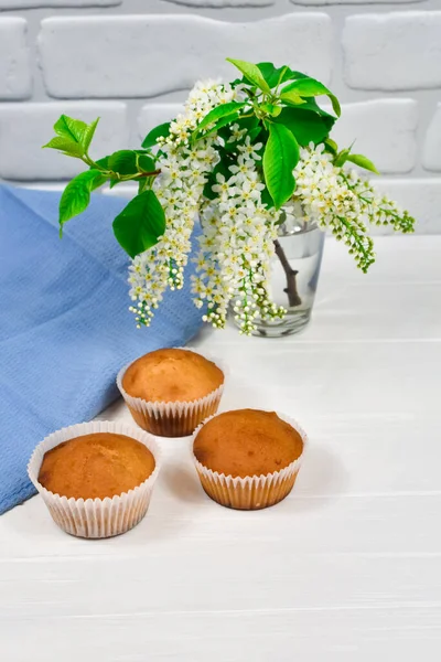 Cupcakes with a bouquet of white flowers. Cupcakes on a white plate with a blue tablecloth and a bouquet of flowers on a white wooden table. — Stock Photo, Image