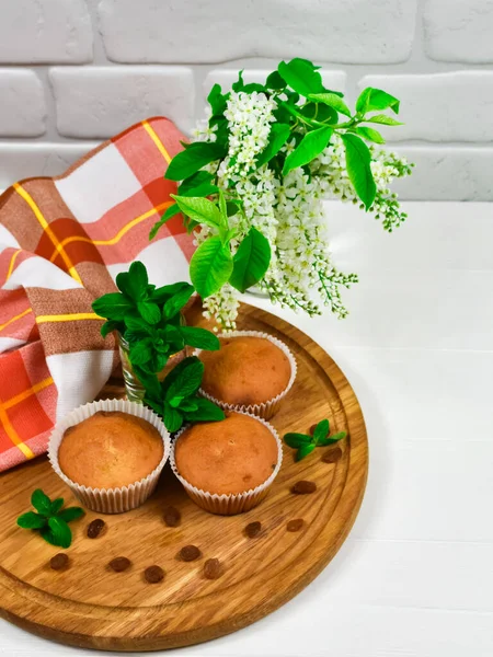 Cupcakes on a wooden board with raisins and a bouquet of white flowers. Three cupcakes on a blackboard with a tablecloth and a bouquet of flowers on a white wooden table. — Stock Photo, Image