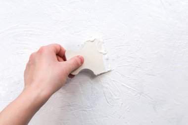 Kadın eli duvara alçı yapıştırıyor. Duvara bir spatulayla alçı yapıştırıyorum..