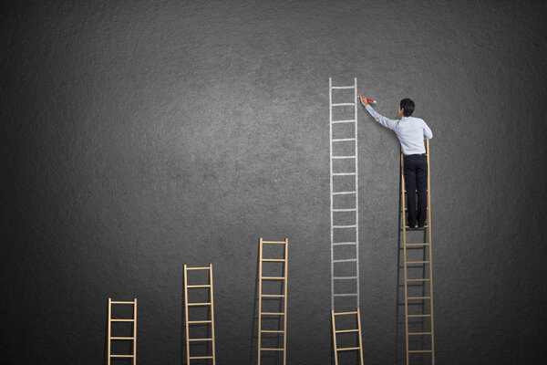 businessman standing on ladder drawing diagrams and graphs